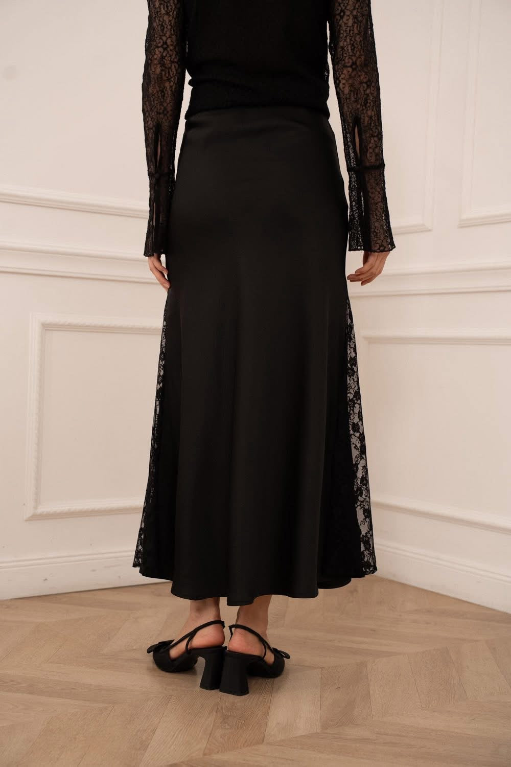 Person wearing a black dress with lace sleeves against a white wall.