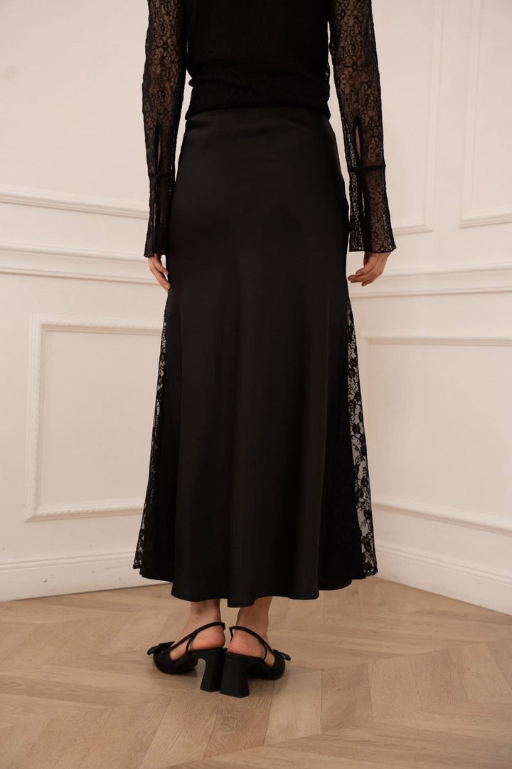 Person wearing a black dress with lace sleeves against a white wall.