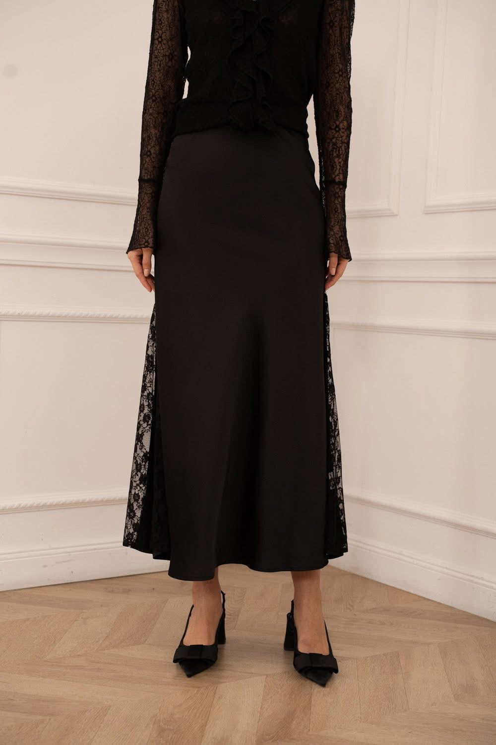 Person wearing a black dress with lace sleeves and hem against a white wall.