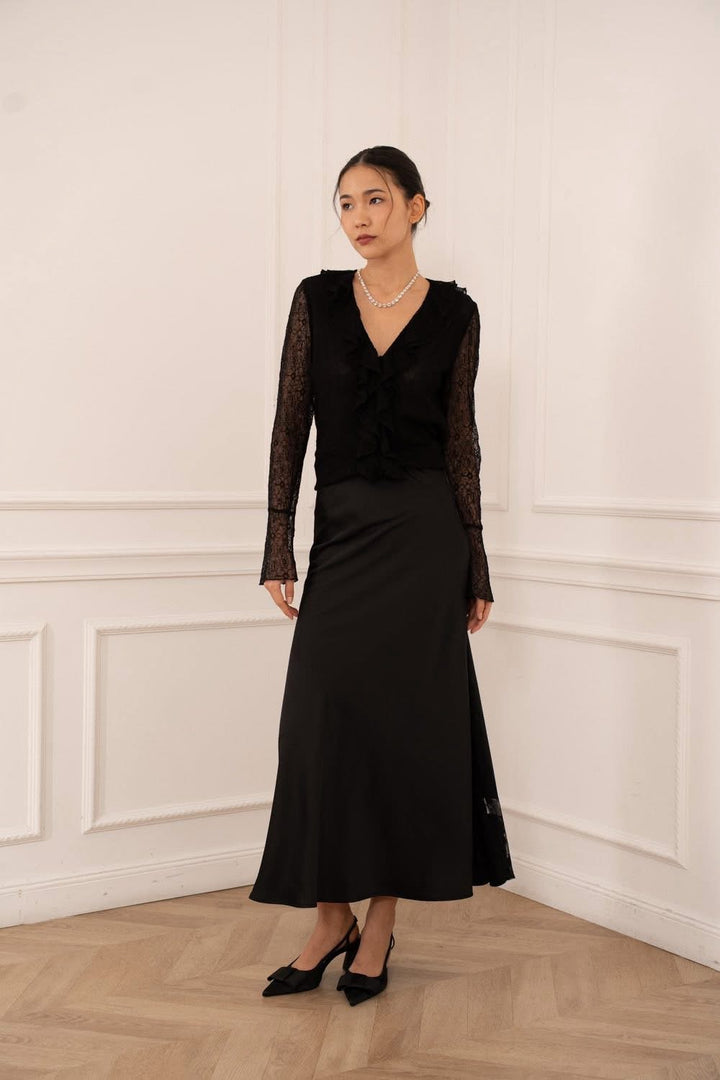 Woman wearing a black dress with lace sleeves against a white wall.