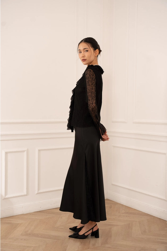 Woman wearing a black outfit with sheer sleeves against a white wall.