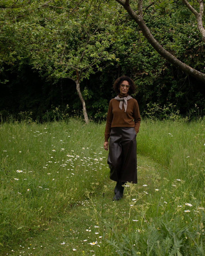 Person walking through a grassy field with trees in the background