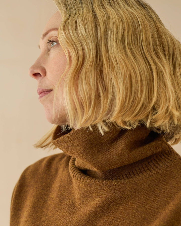 Woman wearing a brown turtleneck sweater against a beige background