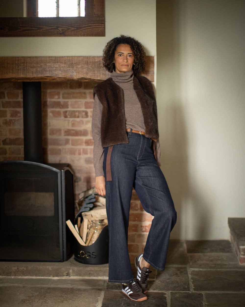 Woman standing in a room with a brick fireplace and wooden logs.