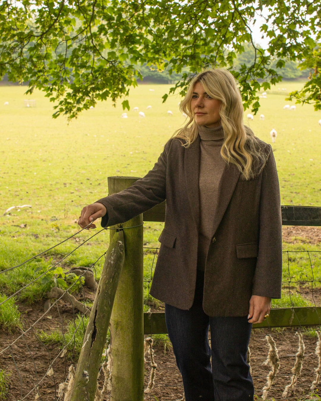 Woman standing by a fence in a field with sheep in the background