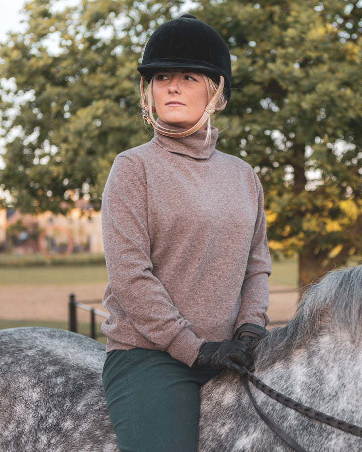 Person in equestrian attire sitting on a horse with trees in the background
