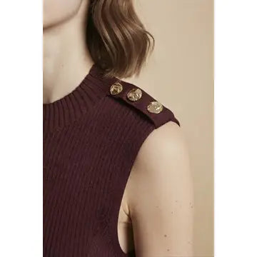 Close-up of a woman wearing a ribbed sleeveless top in deep burgundy with three decorative gold buttons on the shoulder, against a plain beige background.