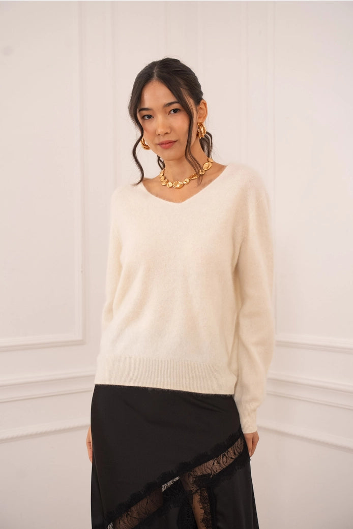 Woman wearing a cream sweater and black skirt against a white wall