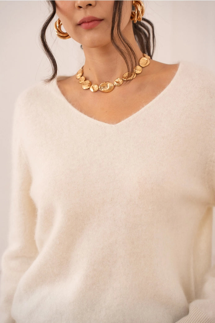 Person wearing a gold necklace and earrings with a plain background