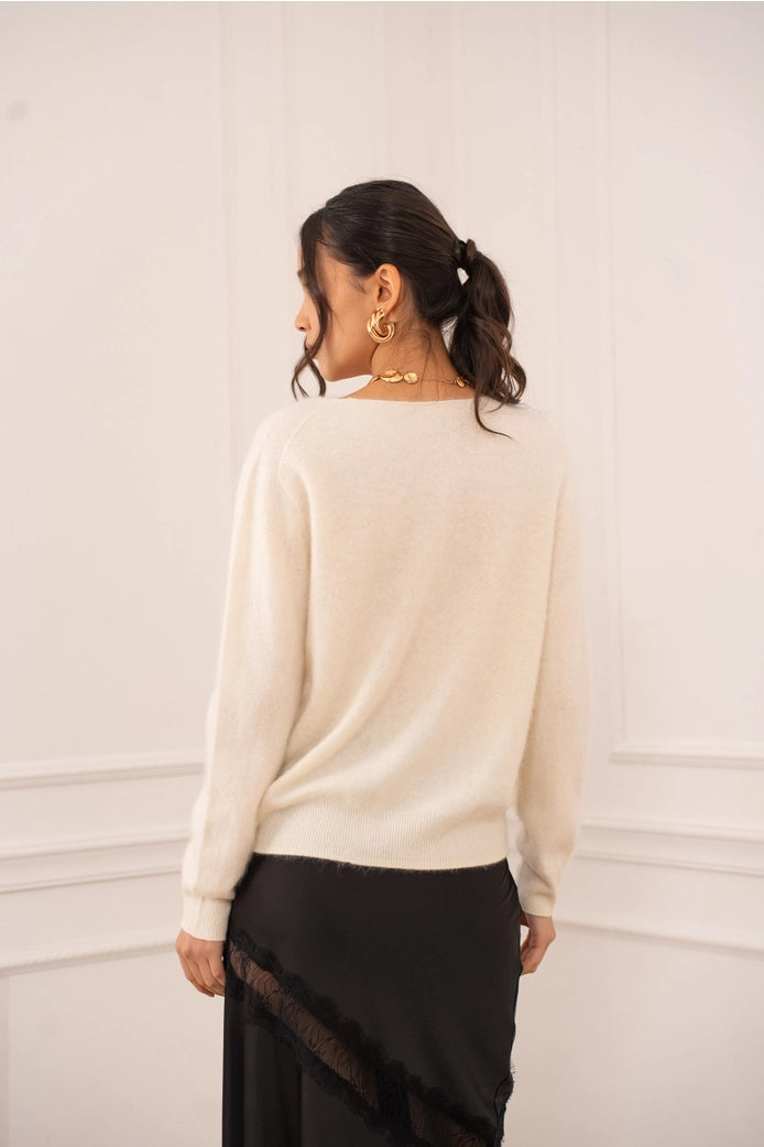 Woman wearing a cream sweater and black skirt against a white wall