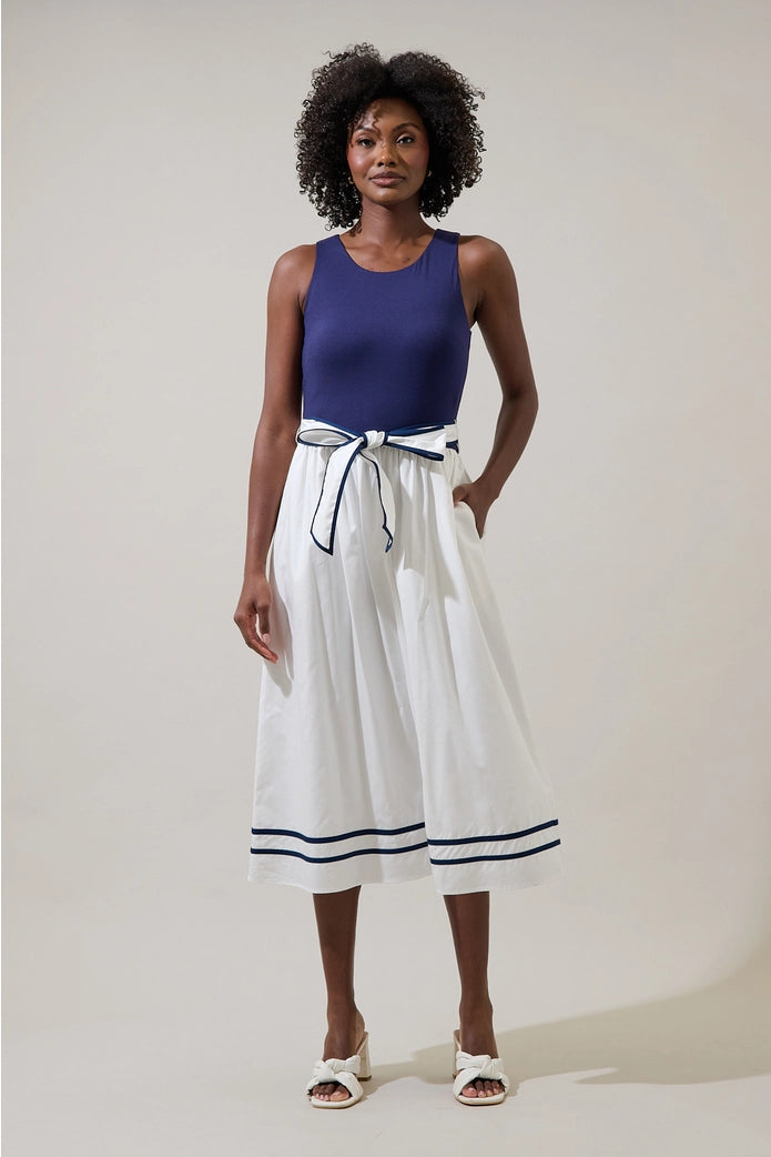 Woman wearing a blue top and white skirt with black trim against a plain background