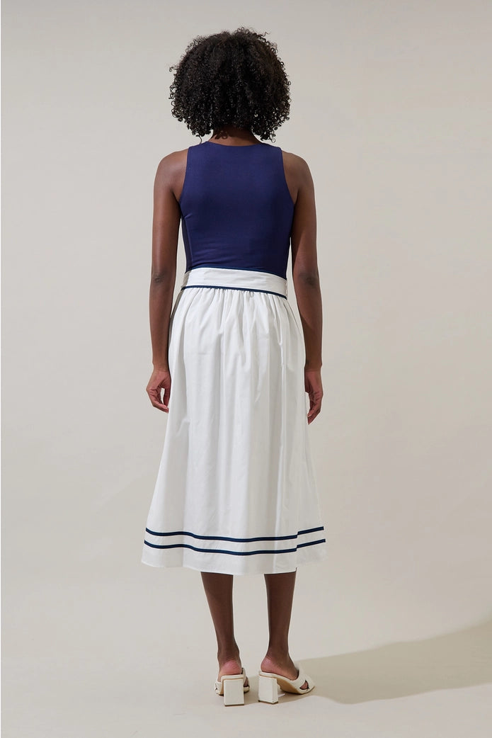 Person wearing a blue top and white skirt with black trim on a plain background