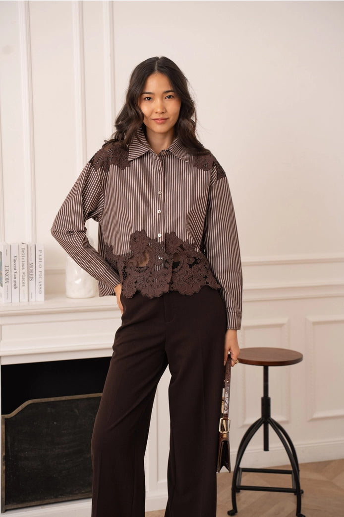 Woman wearing a brown outfit with floral lace details in a room with a fireplace and stool.