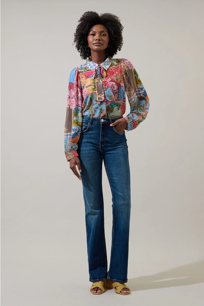 Woman wearing a colorful patterned blouse and blue jeans against a plain background