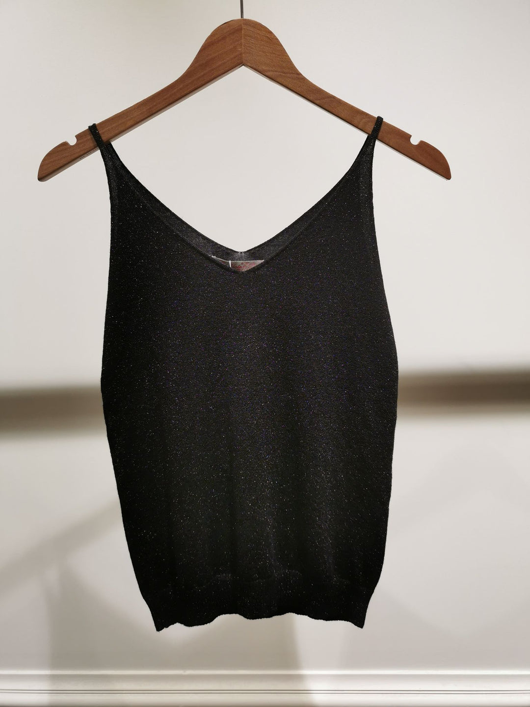Black tank top on a wooden hanger against a white background