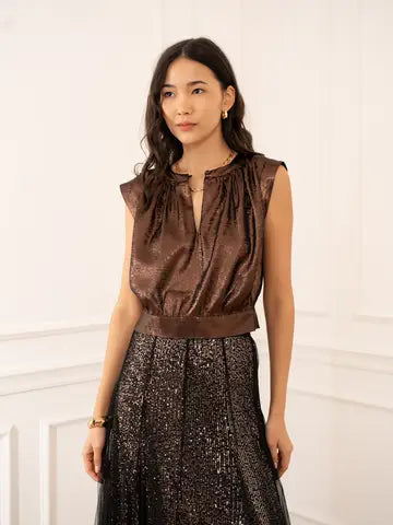 Woman wearing a brown sleeveless top and black sequin skirt against a white wall.