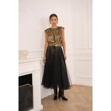 Woman wearing a gold top and black tulle skirt in an elegant room.