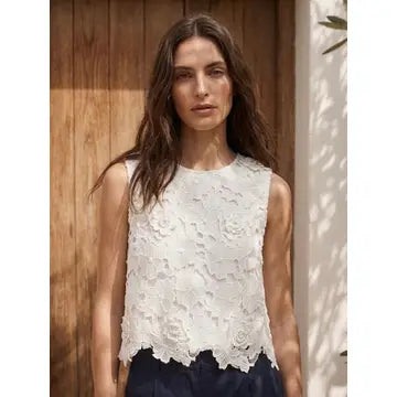 Woman wearing a white lace top standing against a wooden wall.