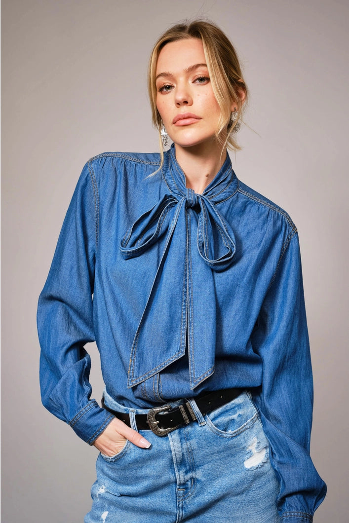 Woman wearing a blue denim shirt with a tie and jeans on a gray background