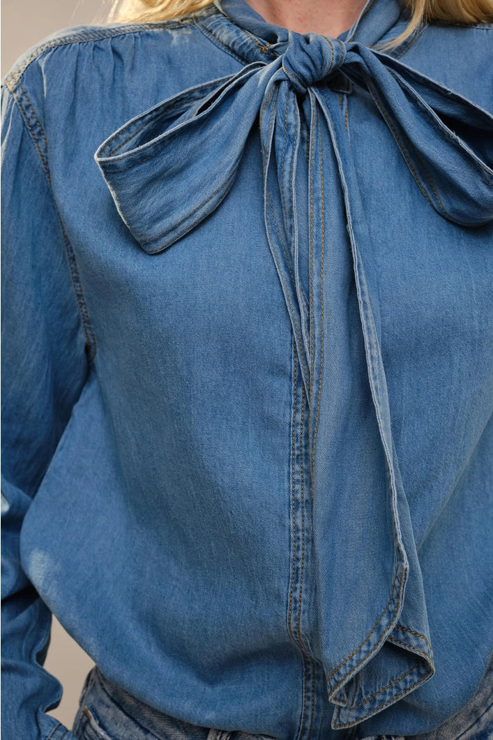 Blue denim blouse with a bow detail on a neutral background