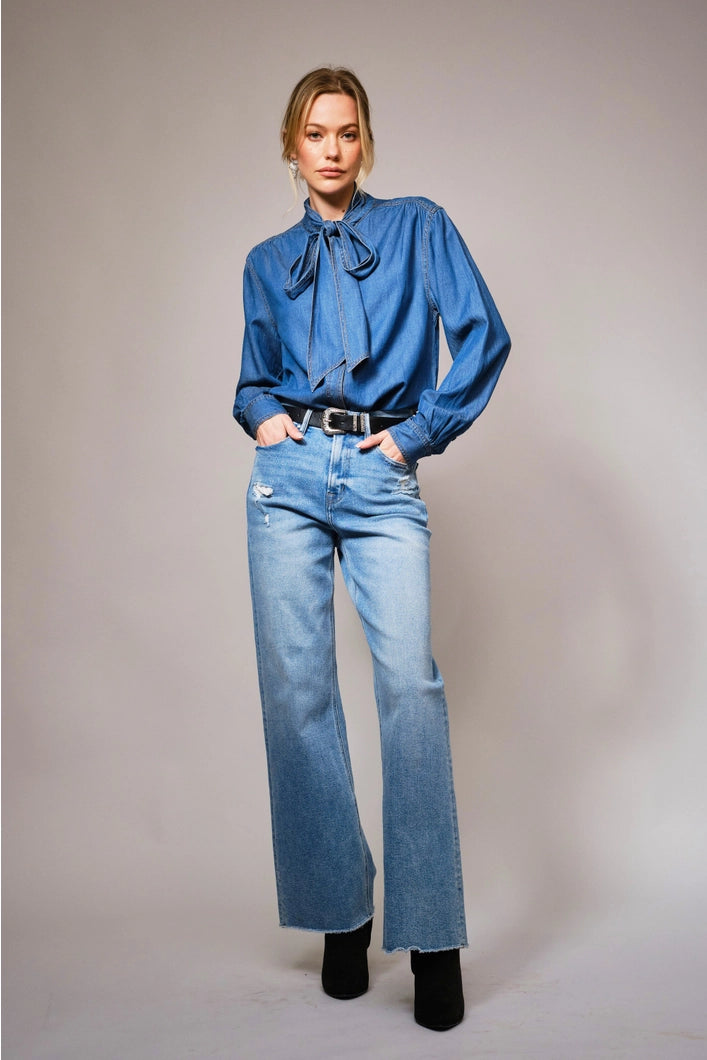 Woman wearing a blue blouse and jeans against a plain background