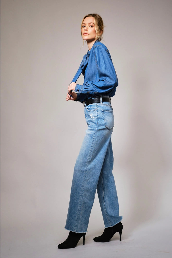 Woman wearing a blue shirt and light blue jeans against a gray background