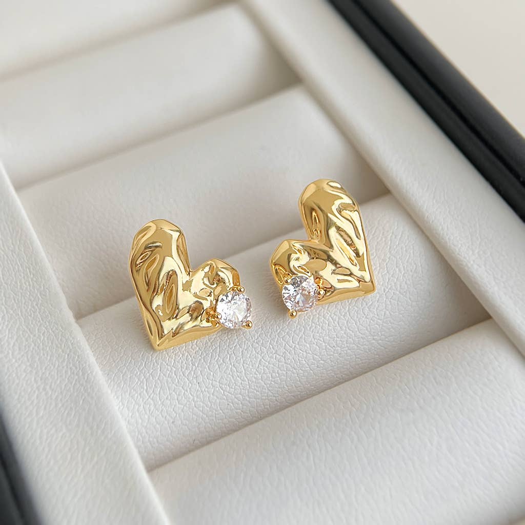 Gold heart-shaped earrings with embedded stones on a light beige background