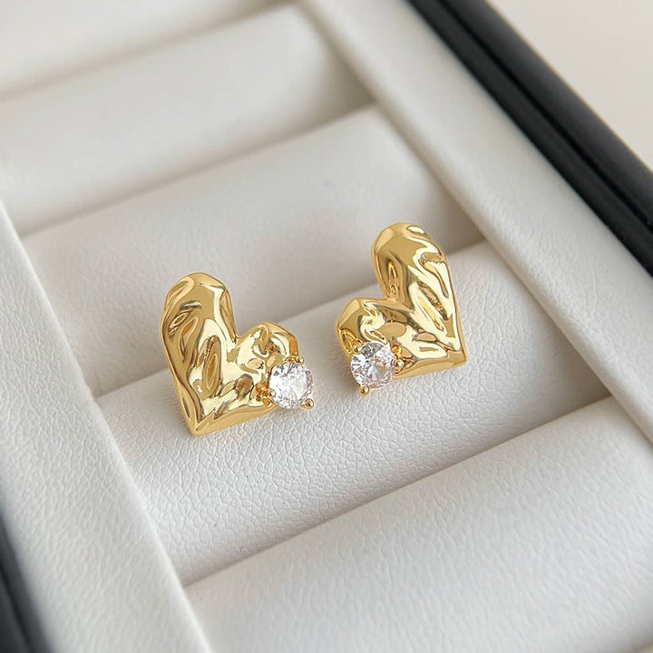 Gold heart-shaped earrings with embedded stones on a light beige background