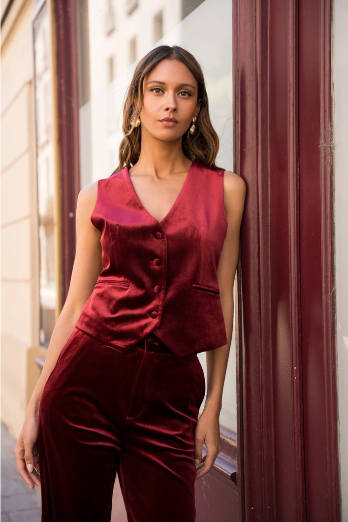 Woman wearing a burgundy velvet outfit standing against a city building background