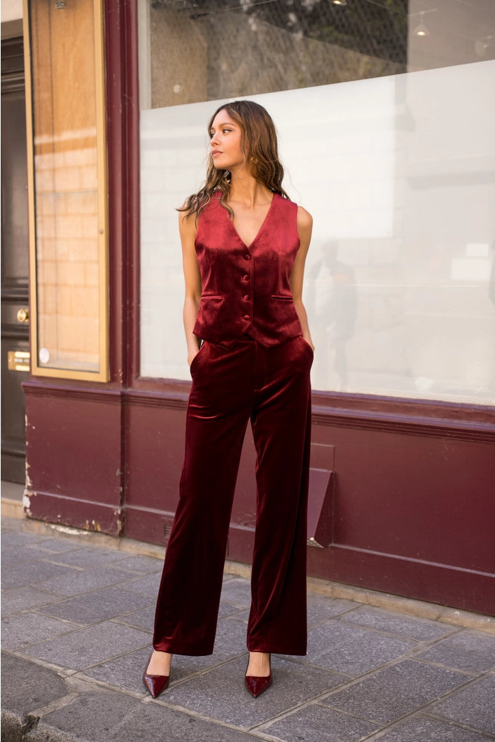 Woman wearing a red velvet jumpsuit standing on a street.