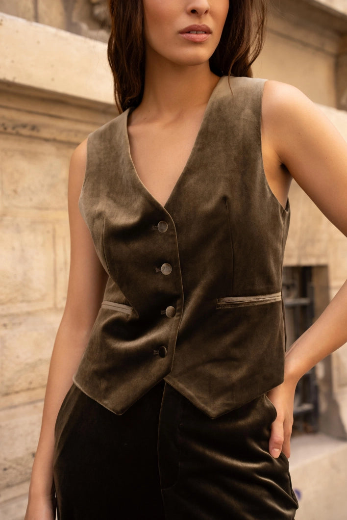 Woman wearing a brown suede vest against a stone wall.