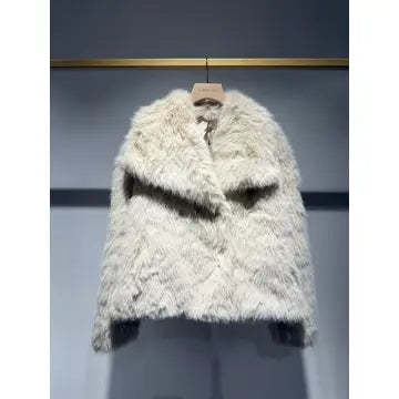 A fluffy faux fur jacket in a light cream or off-white color, hanging on a wooden hanger against a dark gray wall.