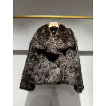 A dark brown and black faux fur jacket hanging on a wooden hanger against a light gray wall with a gold horizontal rod above it.