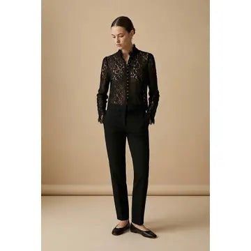 Woman wearing a black lace blouse and black pants against a beige background