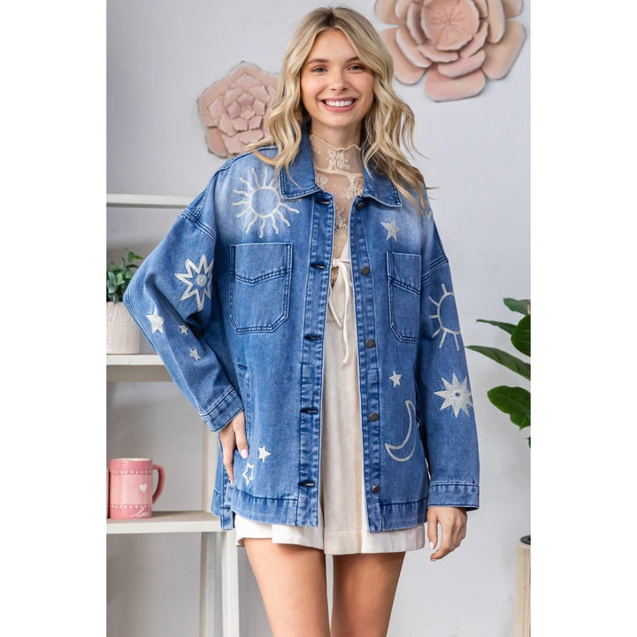 Woman wearing a blue denim jacket with star and moon patterns in a room setting.