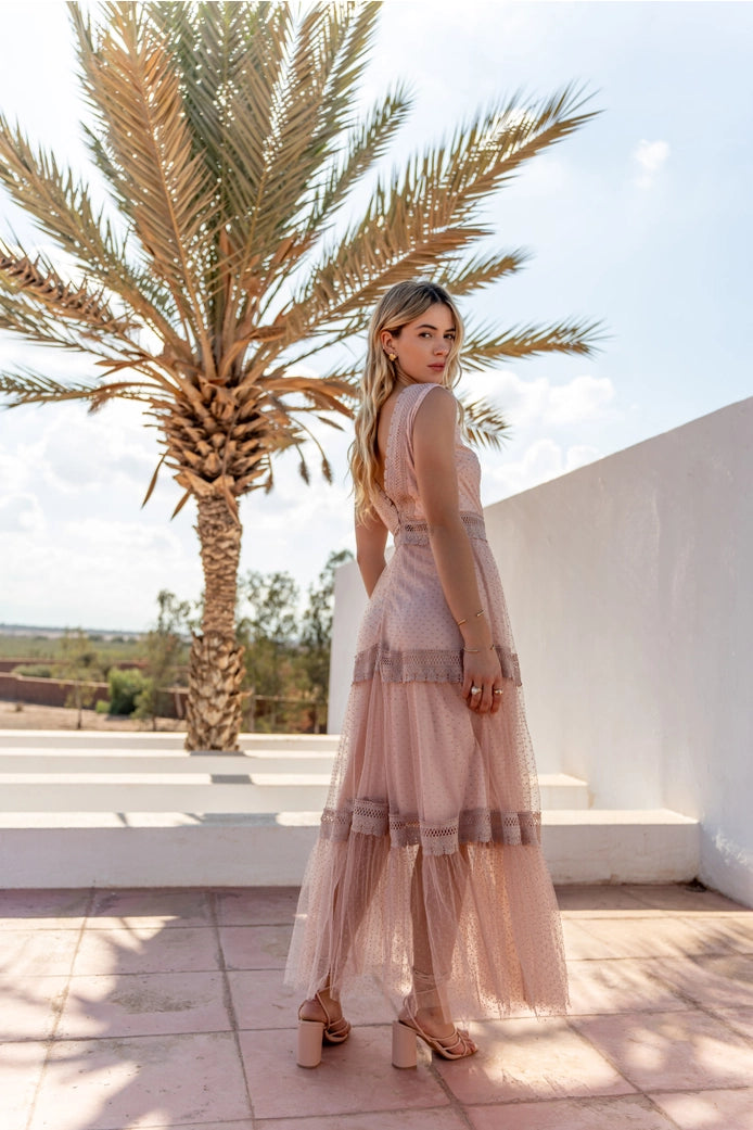Woman in a long, light-colored dress standing on a rooftop with palm trees in the background