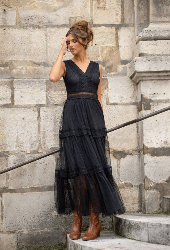 Woman wearing a black dress standing on stone steps against a stone wall.