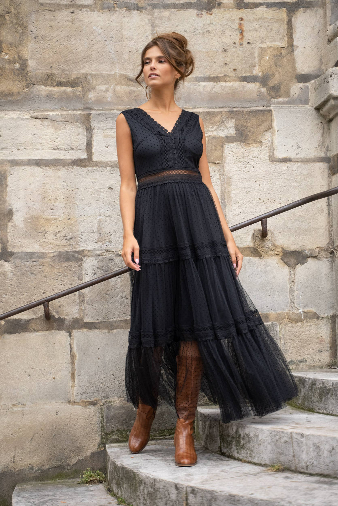 Woman wearing a black dress and brown boots standing on stone steps.