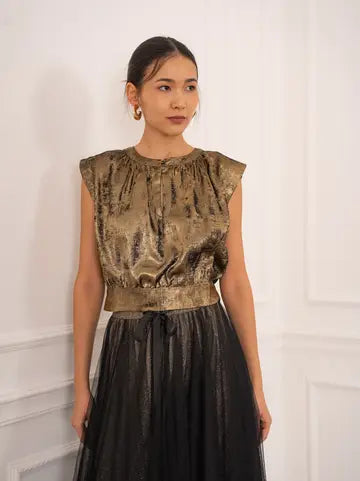Woman wearing a metallic top and black skirt against a white wall