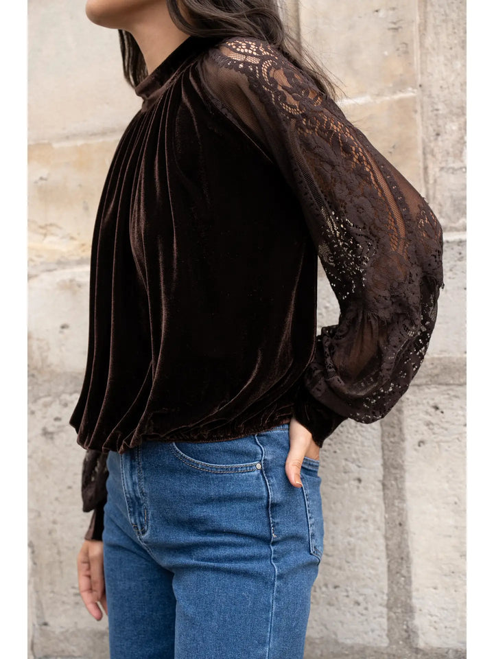 Person wearing a black velvet blouse with sheer lace sleeves against a stone wall.