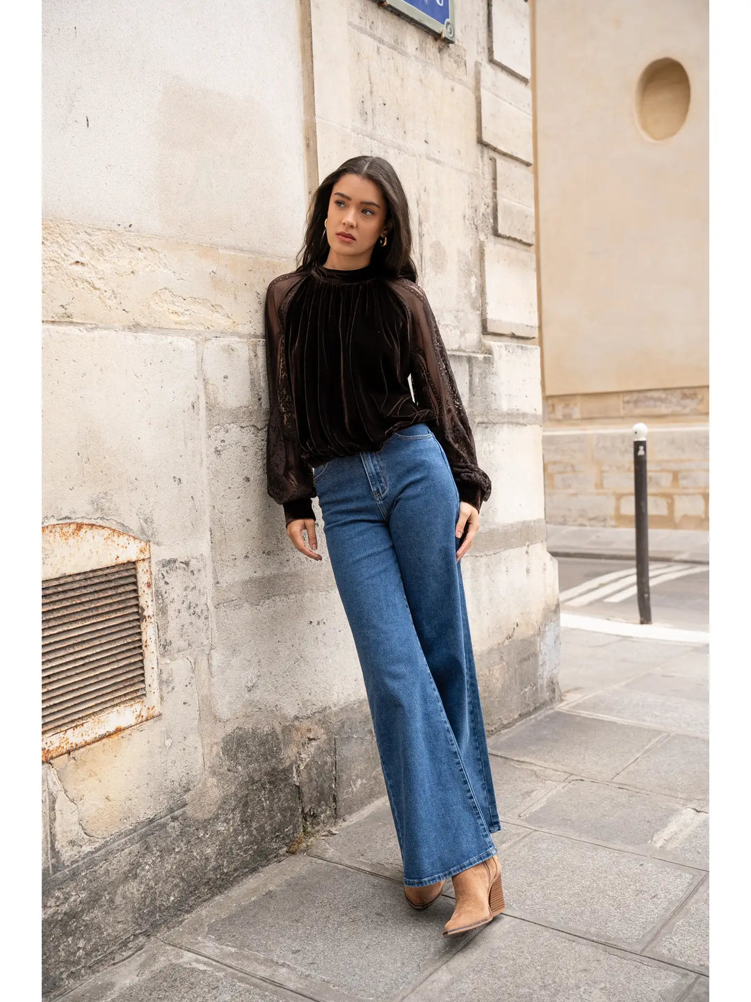 Woman in black sweater and blue jeans standing against a stone wall.