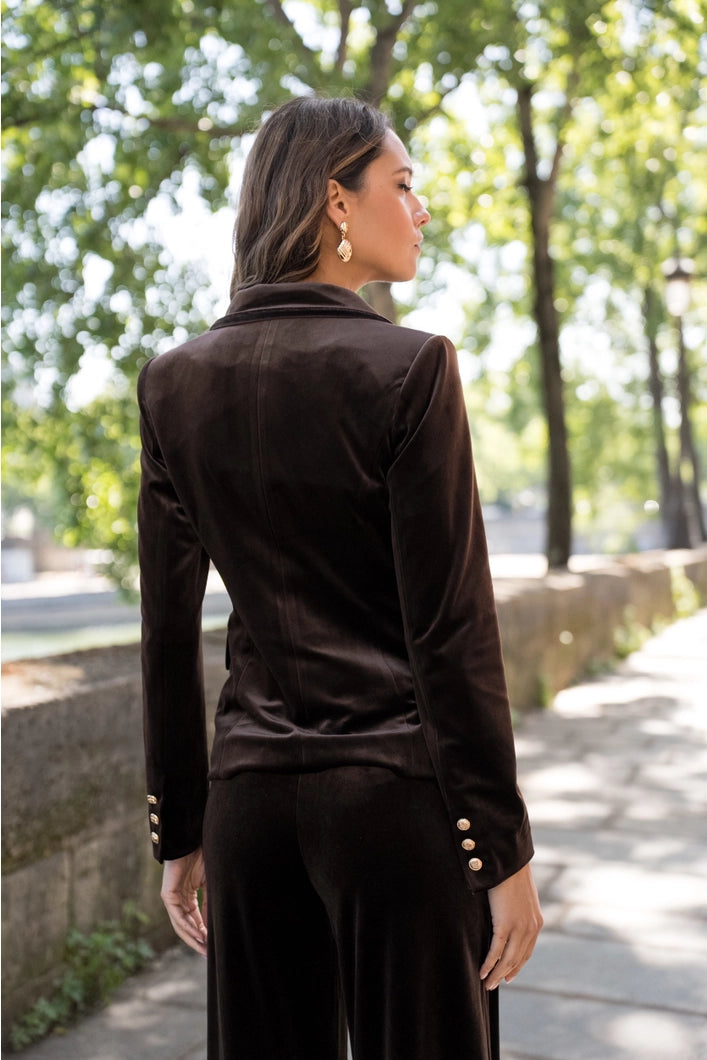 Woman wearing a black jacket and pants walking outdoors with trees in the background