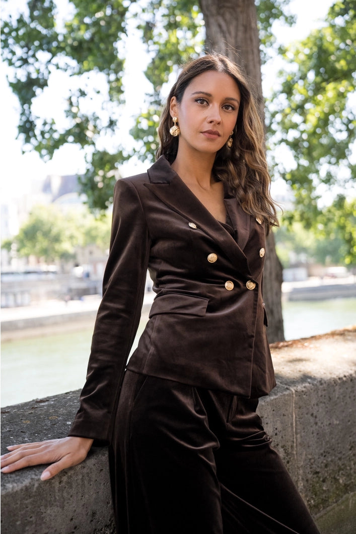 Woman in a brown suit sitting outdoors with trees in the background