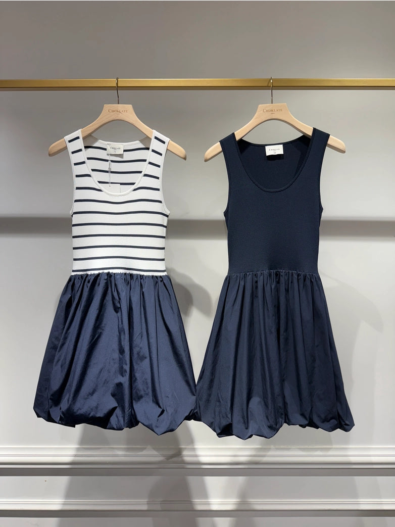 Two navy blue dresses on hangers against a gray background
