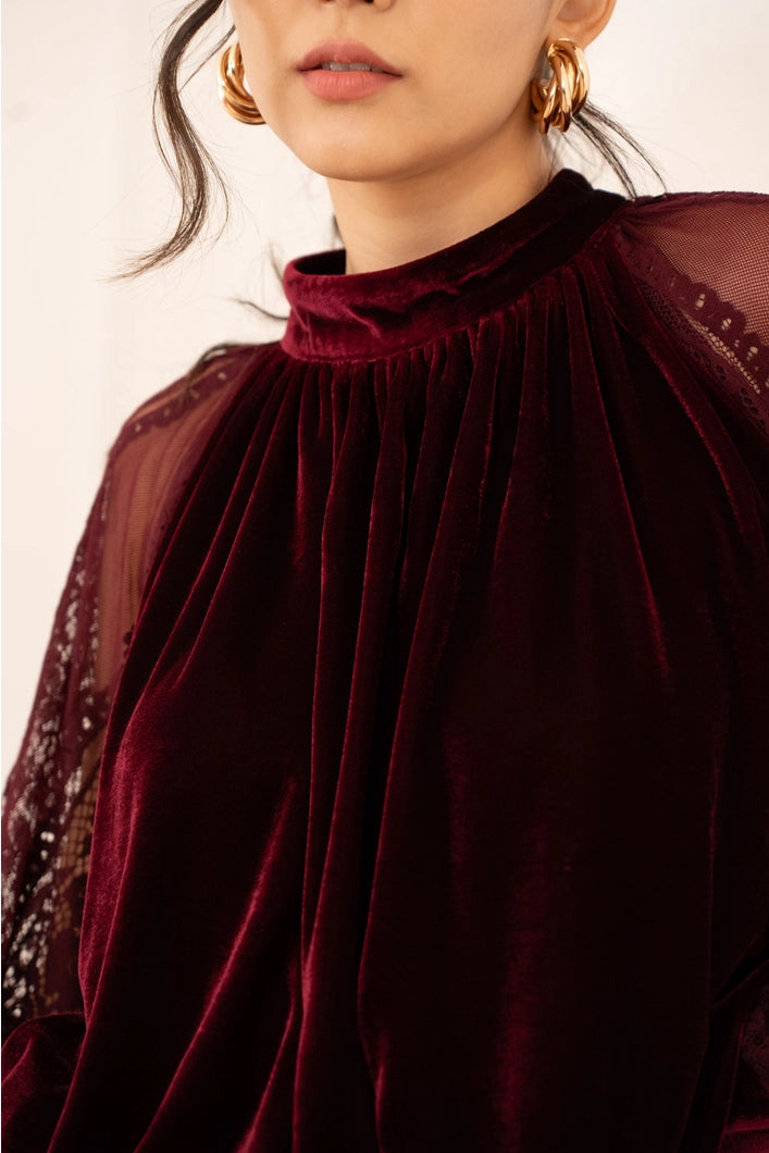 Close-up of a person wearing a burgundy velvet top with sheer sleeves.