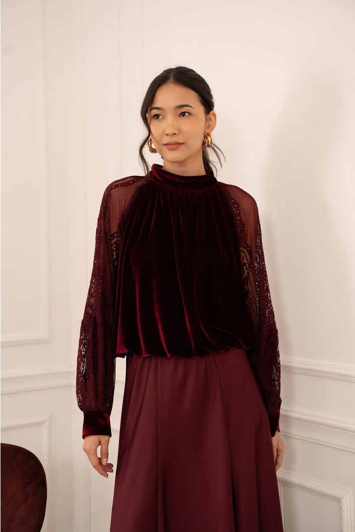 Woman wearing a burgundy top and skirt against a white wall