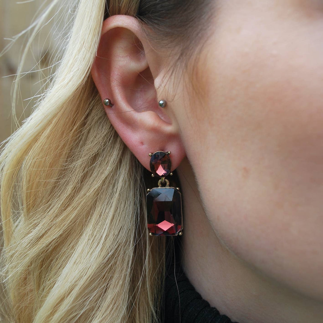 Close-up of an ear wearing a red gemstone earring with blonde hair.