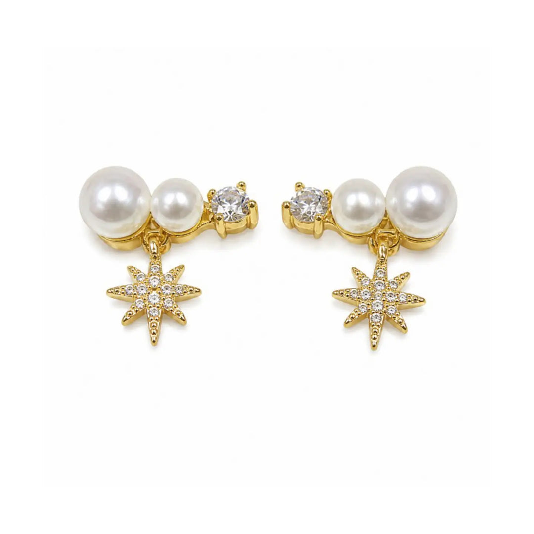 A pair of gold-plated dangle earrings featuring white faux pearls, a small clear crystal, and a dangling gold starburst charm embellished with clear crystals, set against a plain white background.