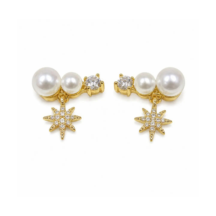 A pair of gold-plated dangle earrings featuring white faux pearls, a small clear crystal, and a dangling gold starburst charm embellished with clear crystals, set against a plain white background.