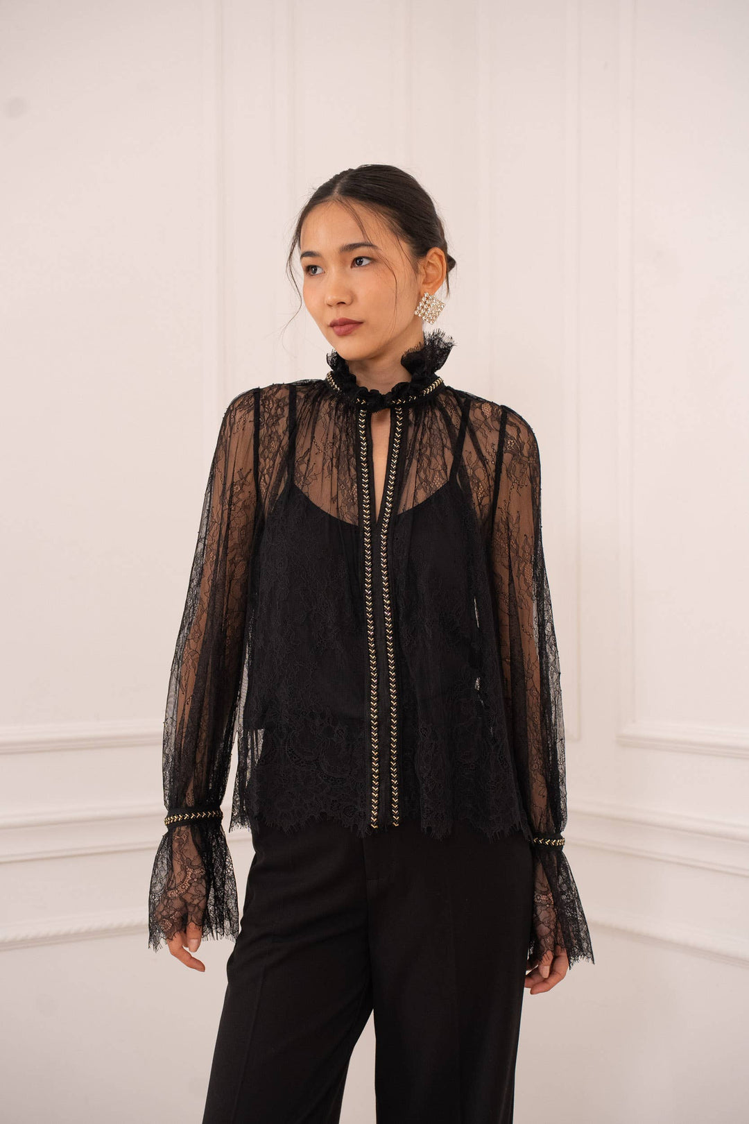 Woman wearing a black lace blouse with sheer sleeves against a white wall
